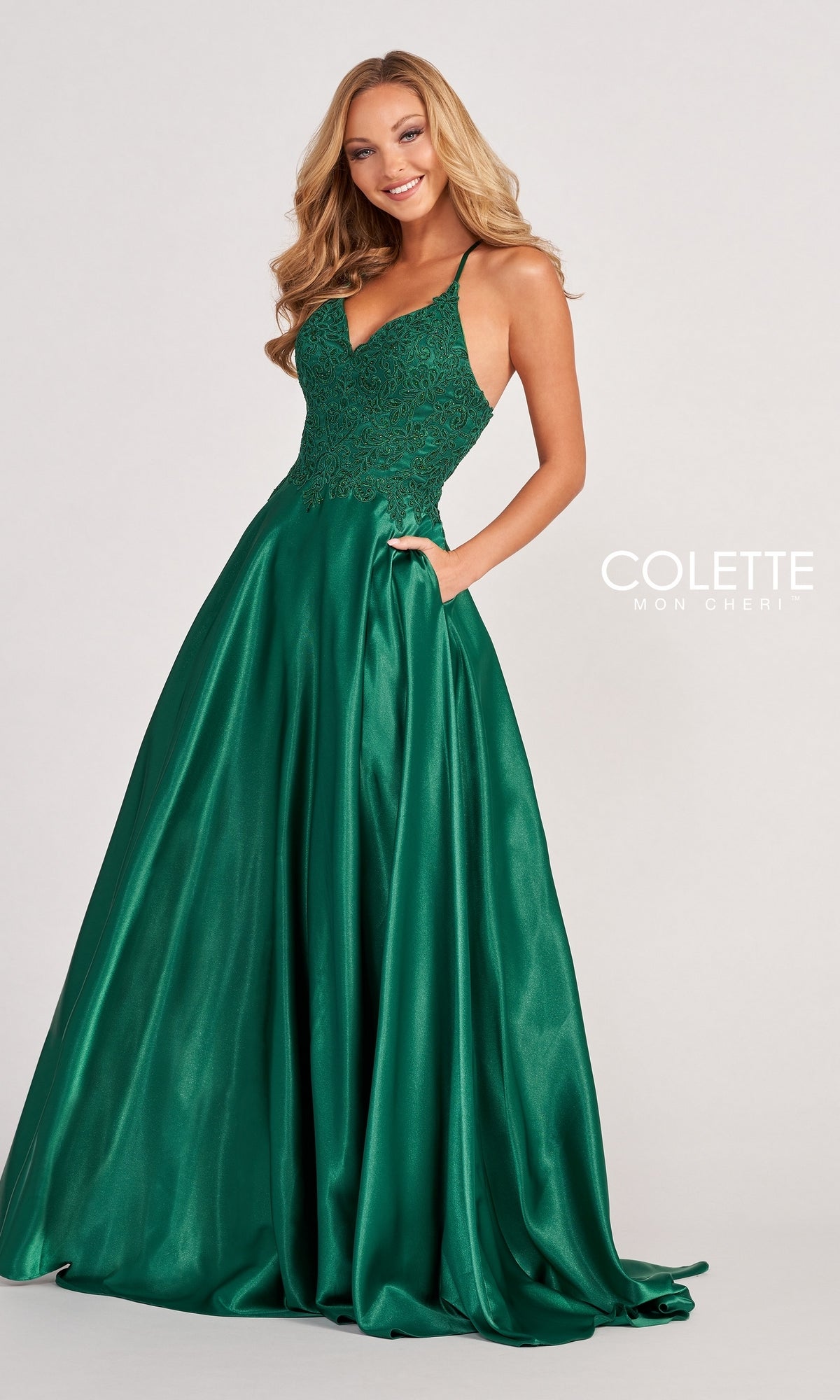A woman wears the Colette by Daphne Satin Prom Ball Gown CL2033, a sleeveless emerald green dress with a fitted lace bodice and full skirt, standing against a plain light background.